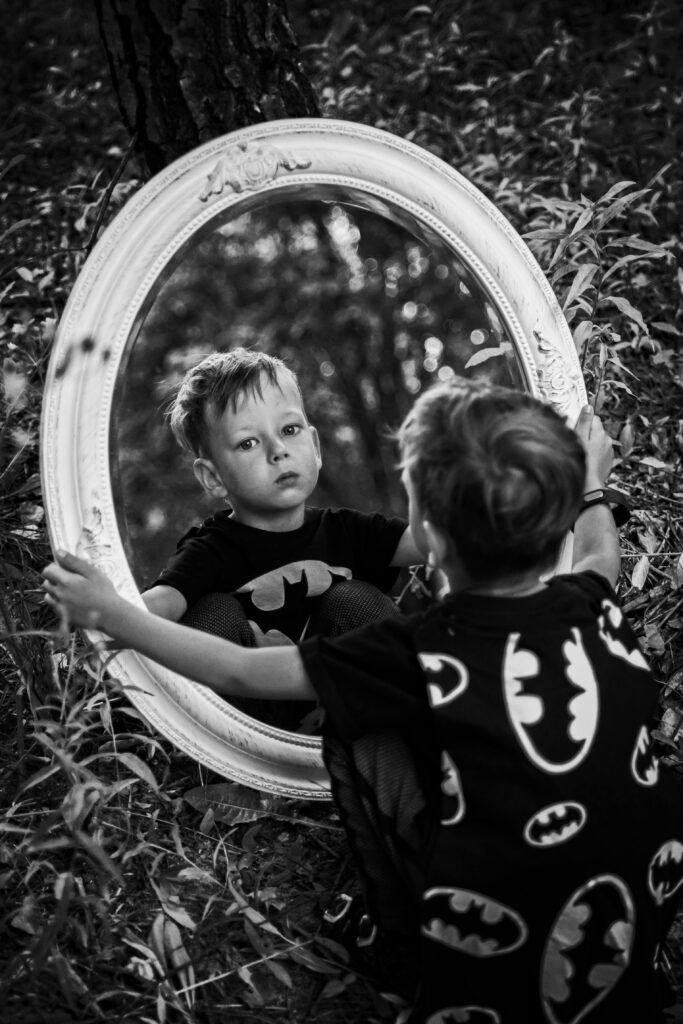 Photo of Little Boy Wearing Batman Cape Looking in a Mirror