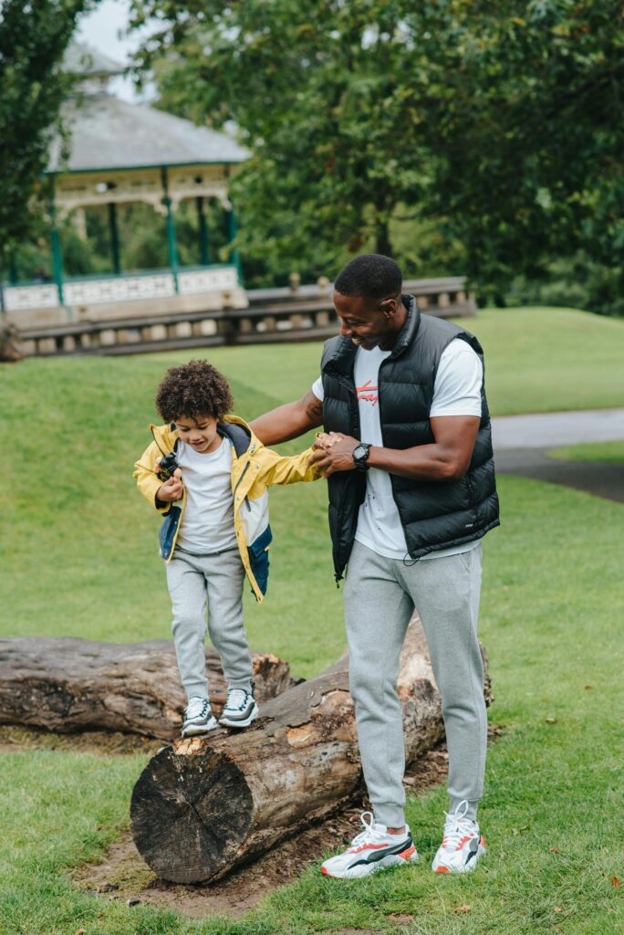 Man Helping a Little Boy Walk on a Log