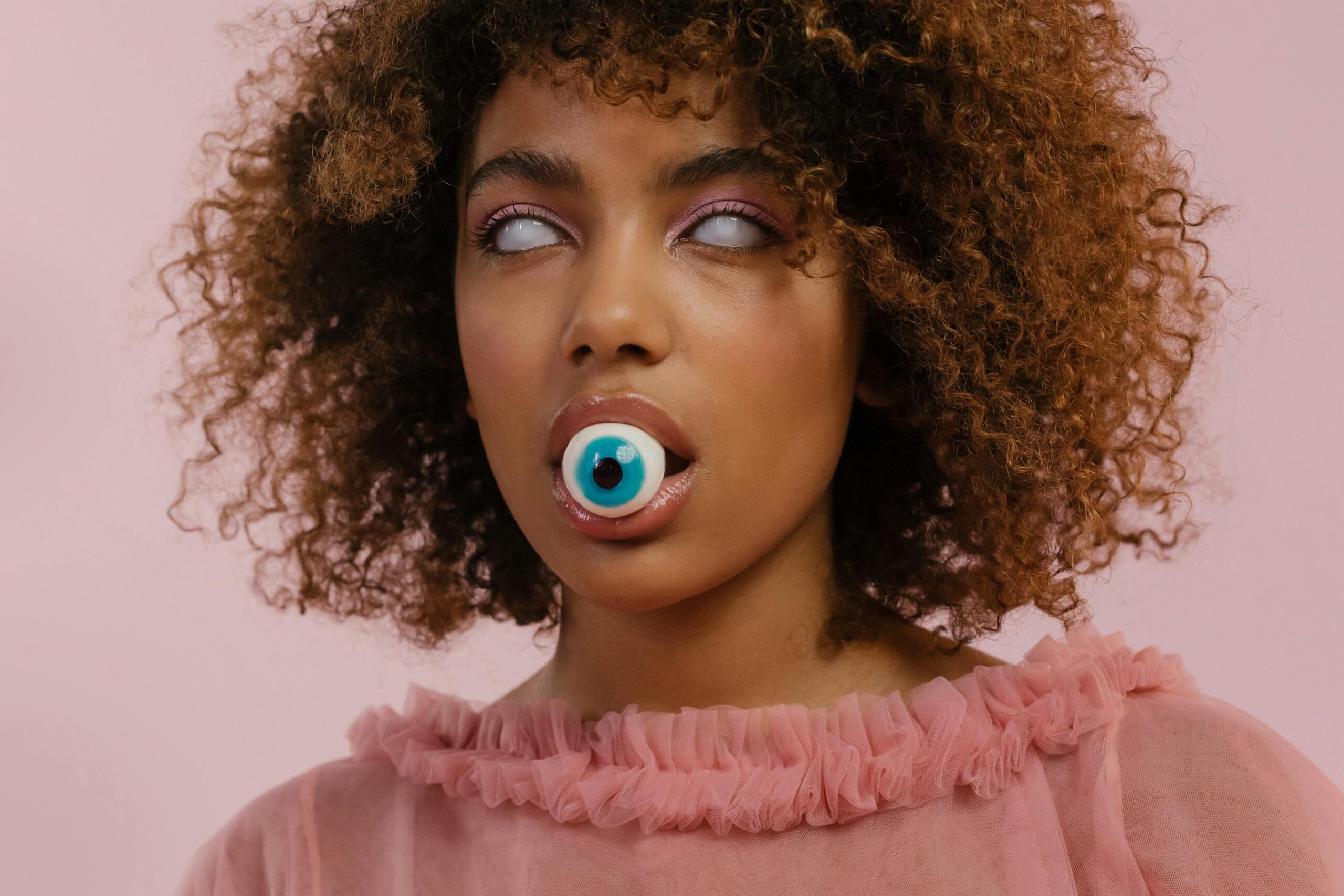 Woman wearing white contacts with a ball resembling an eye in her mouth