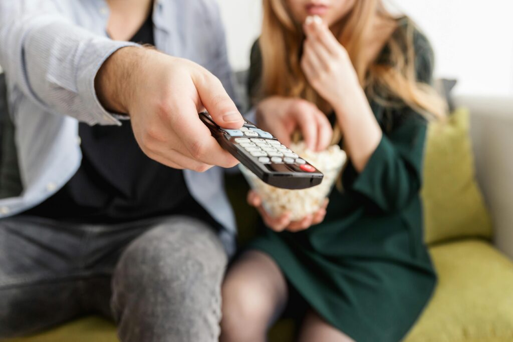 People Holding a Remote and Bowl of Pop Corn